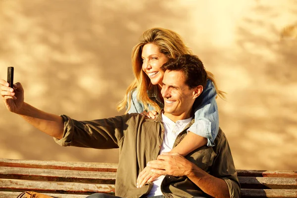 幸福的男朋友和女朋友的画像坐在公园长凳上采取自拍 — 图库照片