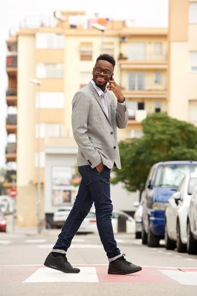 Full length side portrait of young african businessman walking and talking on cell phone in the city