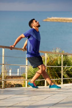 Denizin kenarında germe egzersiz yaparak uygun genç adam tam uzunlukta portresi