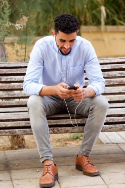 Hareket eden telefon ve kulaklık ile müzik dinlemek bankta oturmuş bir serin Kuzey Afrika genç portresi