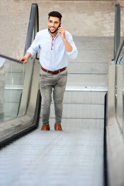 Portrait of handsome arabic man on escalator talking on mobile phone