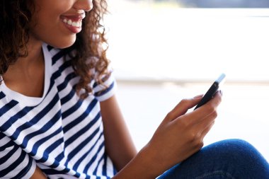 Gülümseyen ve cep telefonuyla mutlu genç siyah güzel kadın portresi kapatın