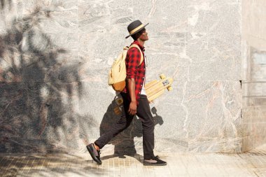 Tam uzunlukta yan dışında kaykay ile yürüyen genç Afro-Amerikan adam portresi