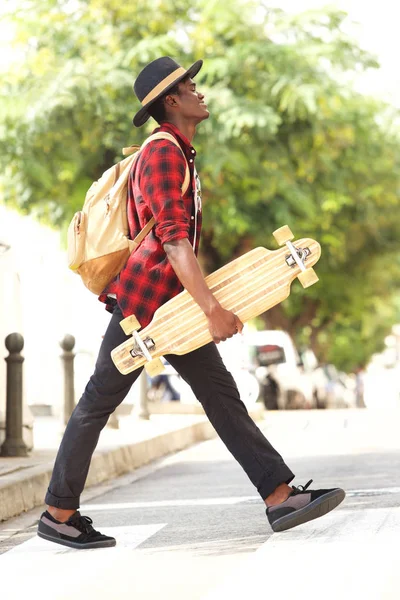 全长侧面的酷年轻非洲家伙在帽子散步户外滑板和袋 — 图库照片