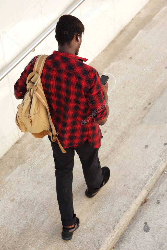 Portrait from above of african male student walking outside using cell phone
