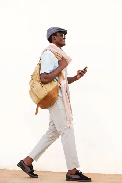 携帯電話と歩いて笑顔のアフリカ系アメリカ人の完全な長さの側肖像画 — ストック写真