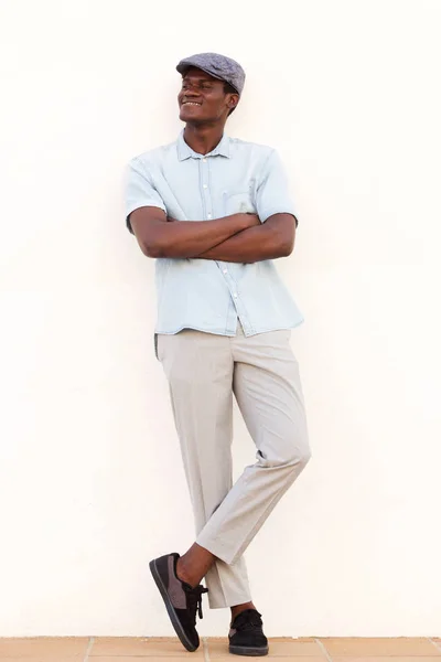 白い壁に寄りかかって腕を組んでクールな若いアフリカ人の完全な長さの肖像画 — ストック写真