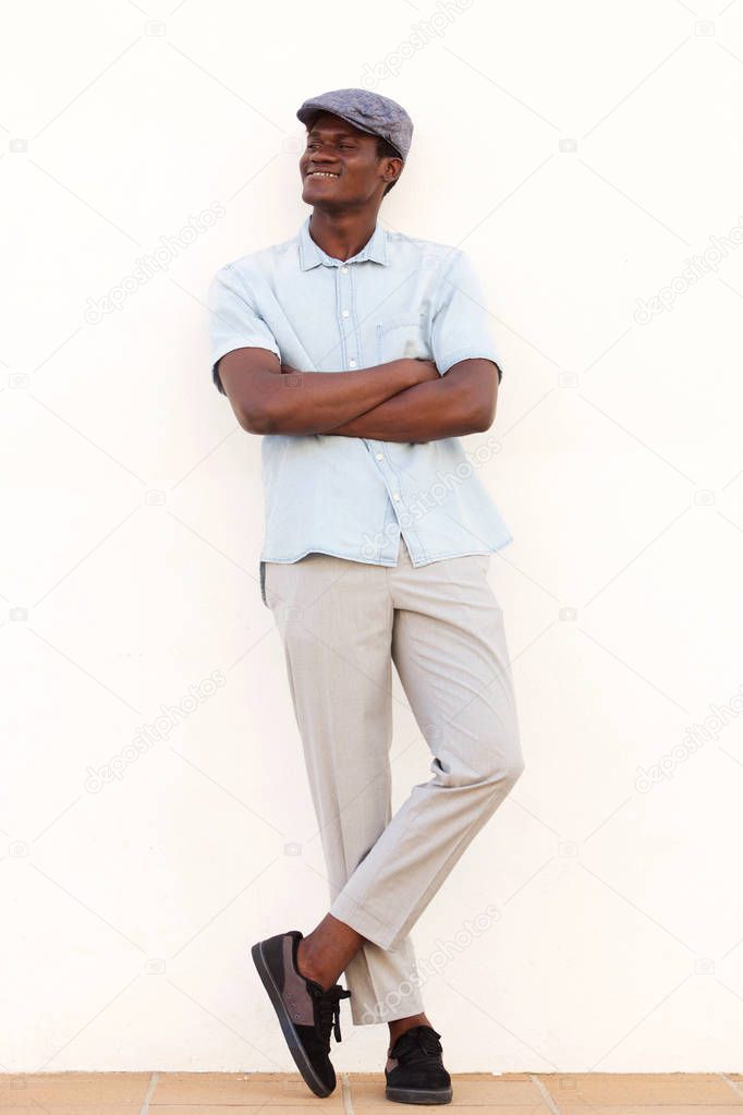 Full length portrait of cool young african man leaning against white wall with arms crossed