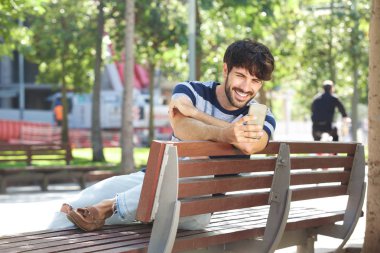 Park smartphone ile gülümseyen yakışıklı genç adam portresi