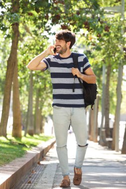 Smartphone ile yürüyen mutlu adam portresi vücut tam ve parkta çanta