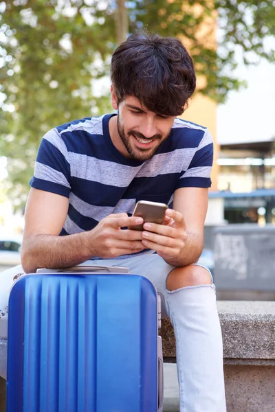 Retrato Jovem Sentado Com Mala Olhando Para Smartphone — Fotografia de Stock