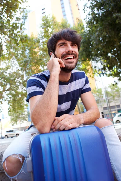 Portrait of handsome young man sitting with mobile phone and suitcase