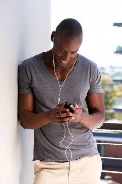 Portre serin bir Afrikalı-Amerikalı adam duvara yaslanmış ve akıllı telefon ile müzik dinlemek