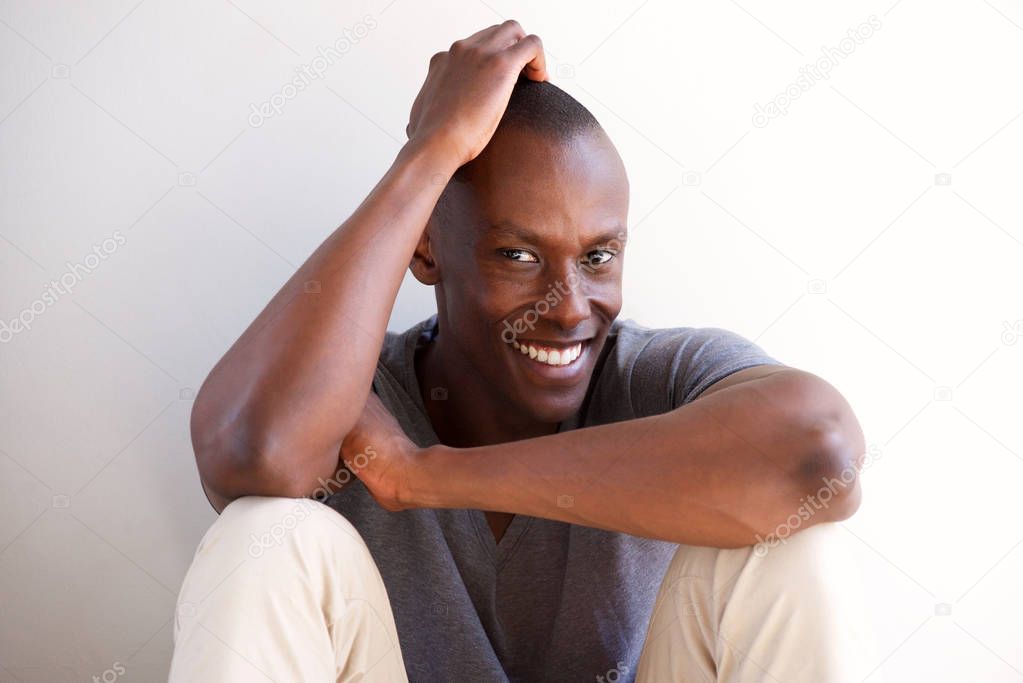 Portrait of smiling young african american man sitting by white wall and thinking