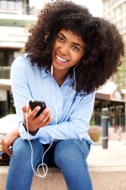 Akıllı telefon ve kulaklık ile dışarıda gülümseyen Afrikalı-Amerikalı kadın portresi