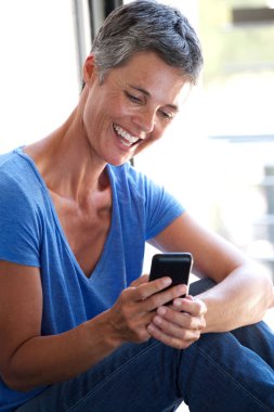 Yan pencere tarafından cep telefonu kullanan mutlu orta yaş kadın portresi