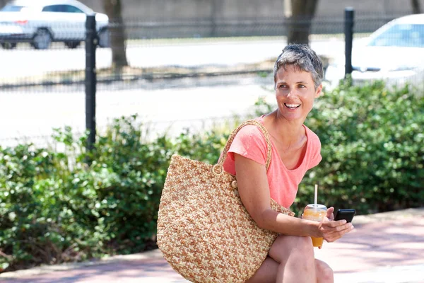ドリンクを屋外に座って 携帯電話を使用して幸せな大人の女性の肖像画 — ストック写真