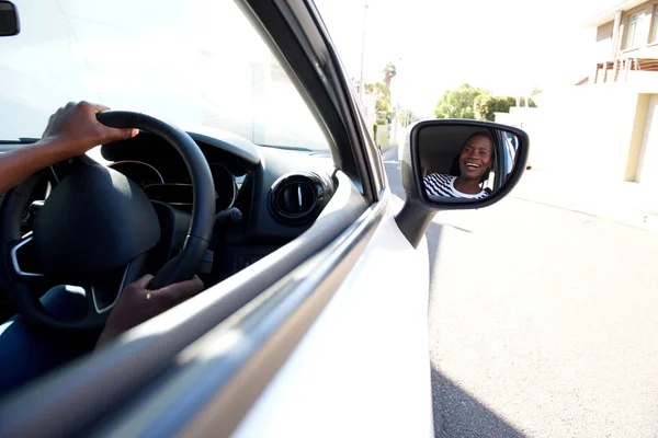 Close up portrait of smiling black woman driving car and looking in side mirror