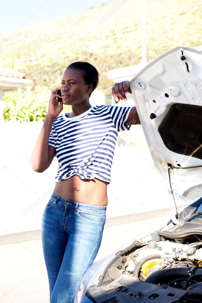 Portrait of black woman standing by broken down car and calling for assistance on mobile phone