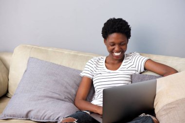 Gülümseyen ve evde kanepede dizüstü kullanarak güzel bir kadın portresi