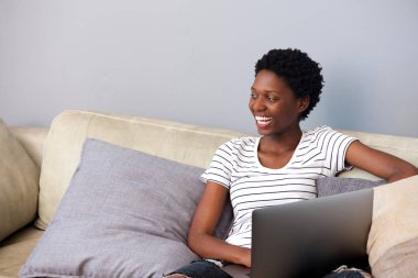 Dizüstü bilgisayar ile kanepede oturan mutlu genç Afrikalı kadın portresi