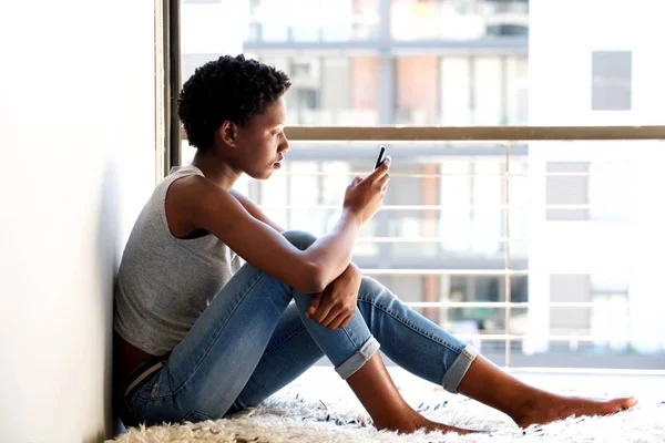 Sida Porträtt Afroamerikanska Kvinna Med Mobiltelefon Genom Fönstret Hemma — Stockfoto