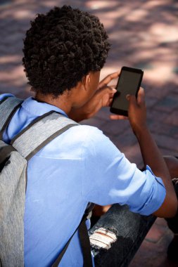 Arkadan portresi akıllı telefon kullanarak dışında oturan kız öğrenci