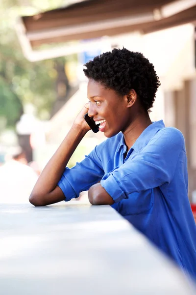 幸せな若い女笑って カフェの外で携帯電話で話しているの側面の肖像画 — ストック写真