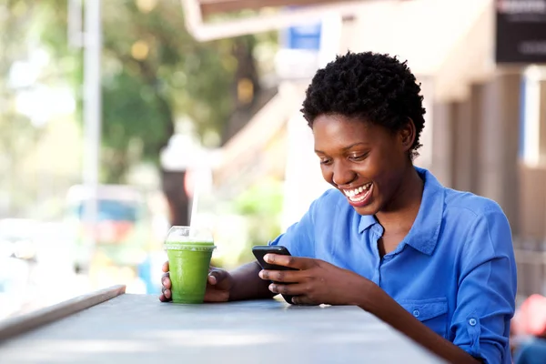 携帯電話を使用して屋外のカフェに座って幸せな若いアフリカ女性の肖像画 — ストック写真