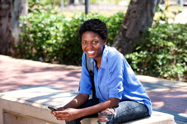 Портрет Улыбающейся Молодой Черной Женщины Сидящей Снаружи Мобильным Телефоном — стоковое фото