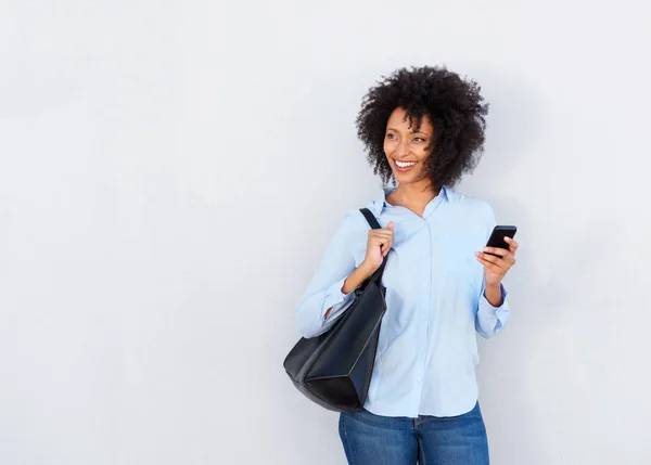 Portrait of attractive black woman with purse and cellphone on gray background