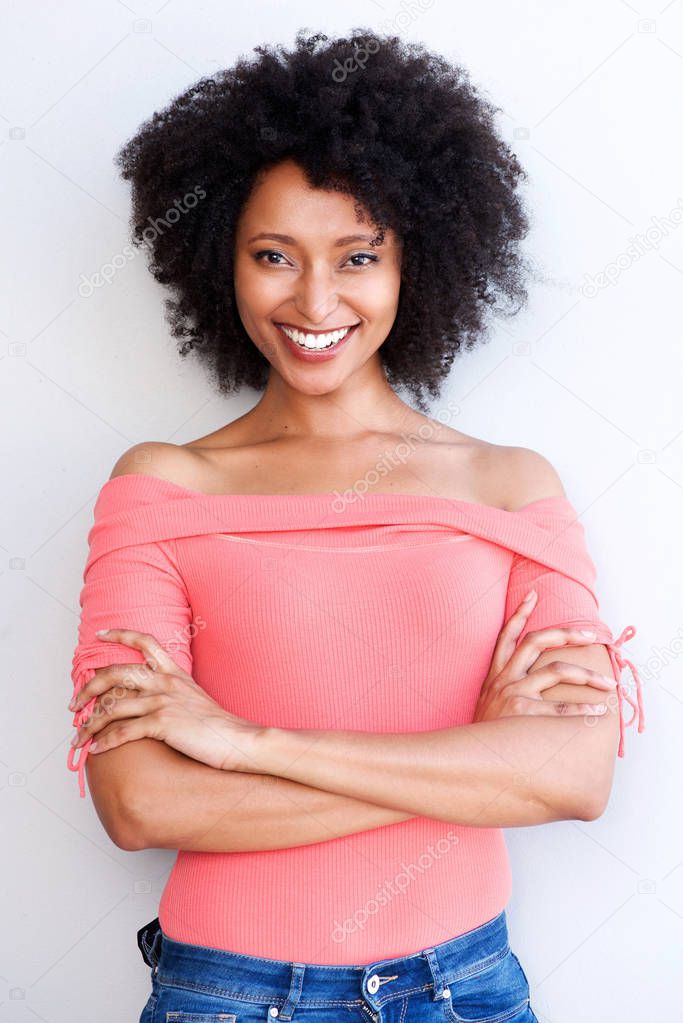 Portrait of attractive young black woman standing with arms crossed and smiling against white background