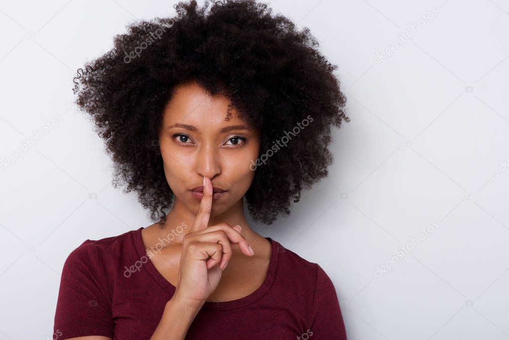 Close up portrait of beautiful young black woman with finger over lips gesturing silence