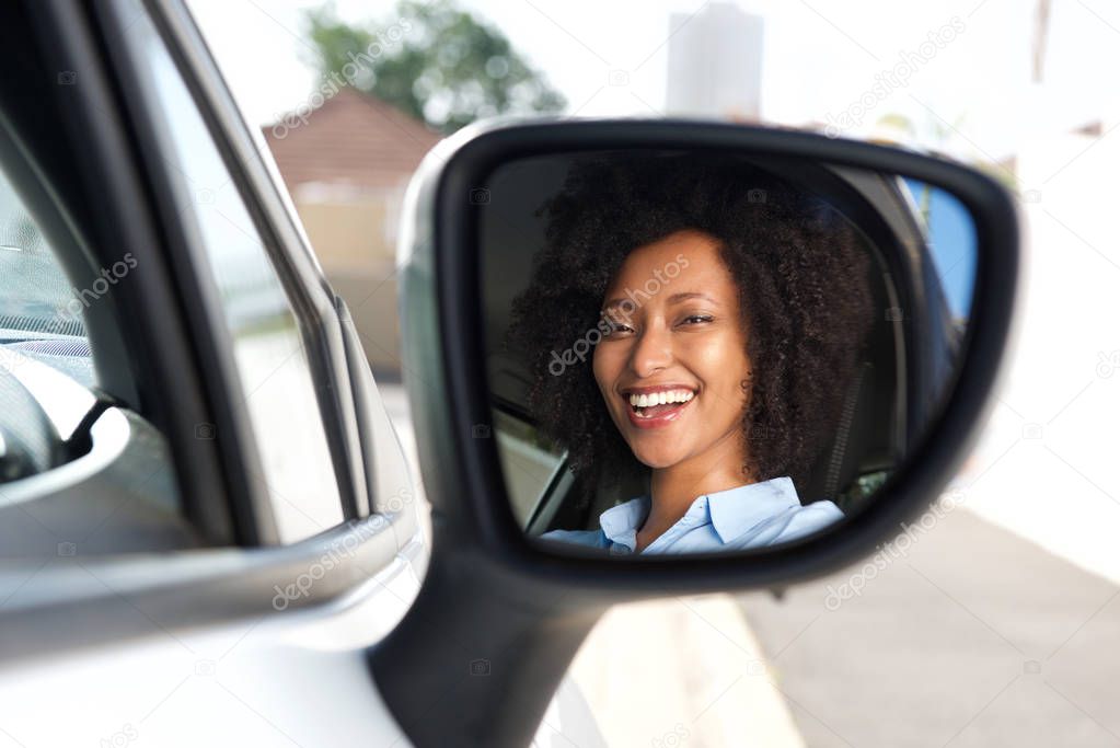 Portrait of reflection in side mirror of smiling african woman driving car