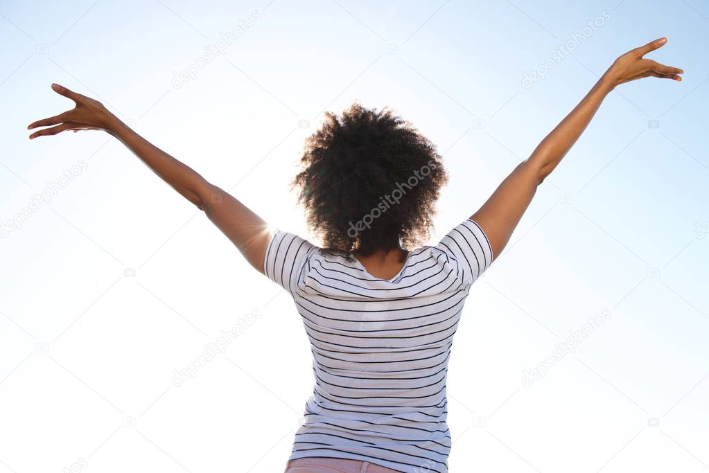 Rear view portrait of young female standing outdoors against sky with her hands raised