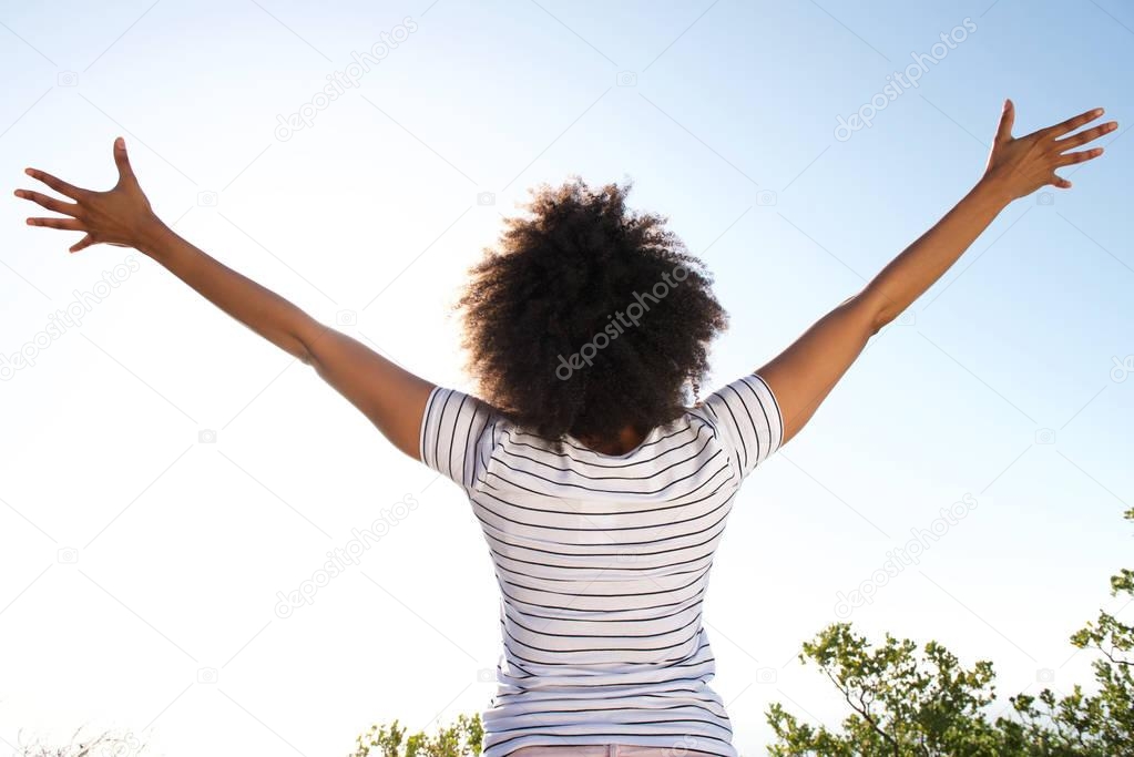 Portrait from behind of young woman looking at sun with arms raised