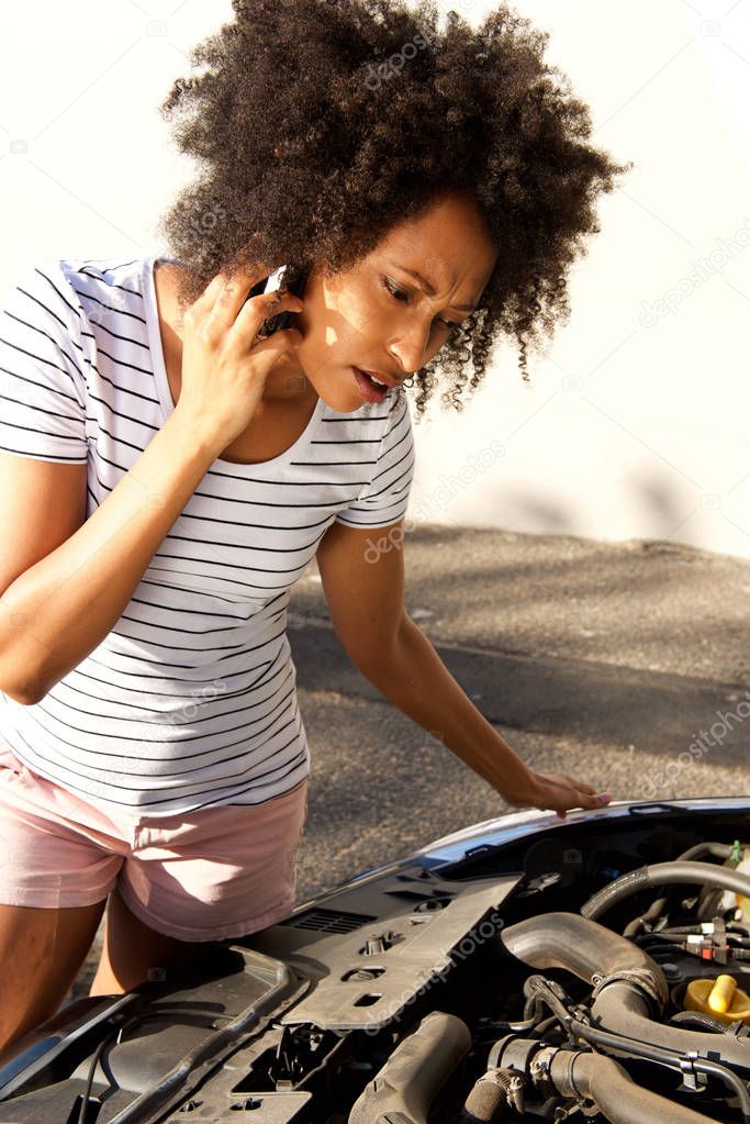 Portrait of african woman looking at her broken car and making phone call for assistance