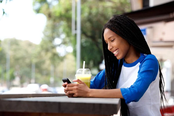 携帯電話を使用して屋外のカフェに座って幸せな若いアフリカ女の側の肖像画 — ストック写真