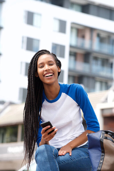 Portrait of beautiful young black woman sitting outdoors with cellphone and smiling