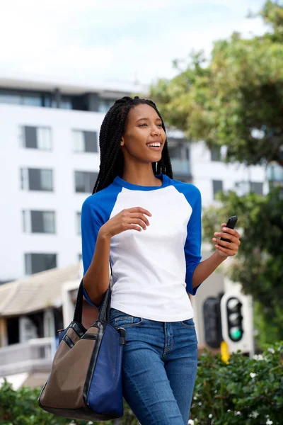 Portrait of happy young african woman walking with bag and mobile phone