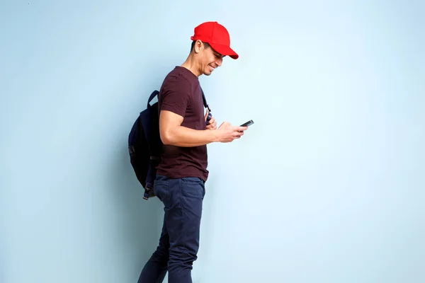 Side portrait of happy mature man with cap and bag looking at his mobile phone and smiling