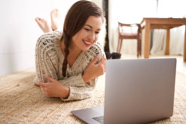 Dizüstü bilgisayar ile yerde yatarken gülümseyen genç kadın portresi