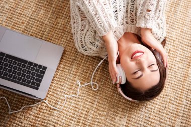 Yukarıdan portresi kulaklık ve dizüstü bilgisayar ile uzanarak gülümseyen genç kadın