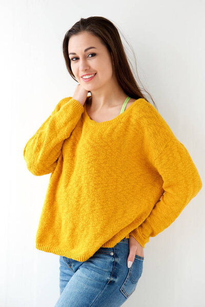 Portrait of attractive young woman smiling in yellow sweater against white wall