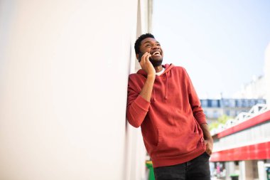 Duvara yaslanmış, cep telefonuyla konuşan mutlu bir Afro-Amerikan portresi.