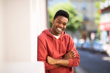 Kollarını kavuşturup duvara yaslanmış gülümseyen Afro-Amerikan bir adam. 