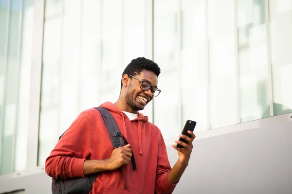 アフリカ系アメリカ人大学生がバッグを持って歩き 携帯電話を見ている姿 — ストック写真