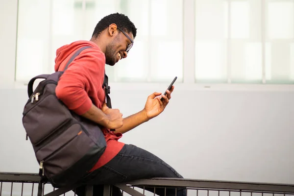 携帯電話を見て外に座っている若いアフリカ系アメリカ人の男性のサイドポートレート — ストック写真