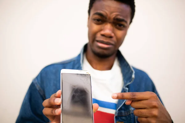 Close up portrait of sad young black man pointing to cracked glass on mobile phone screen