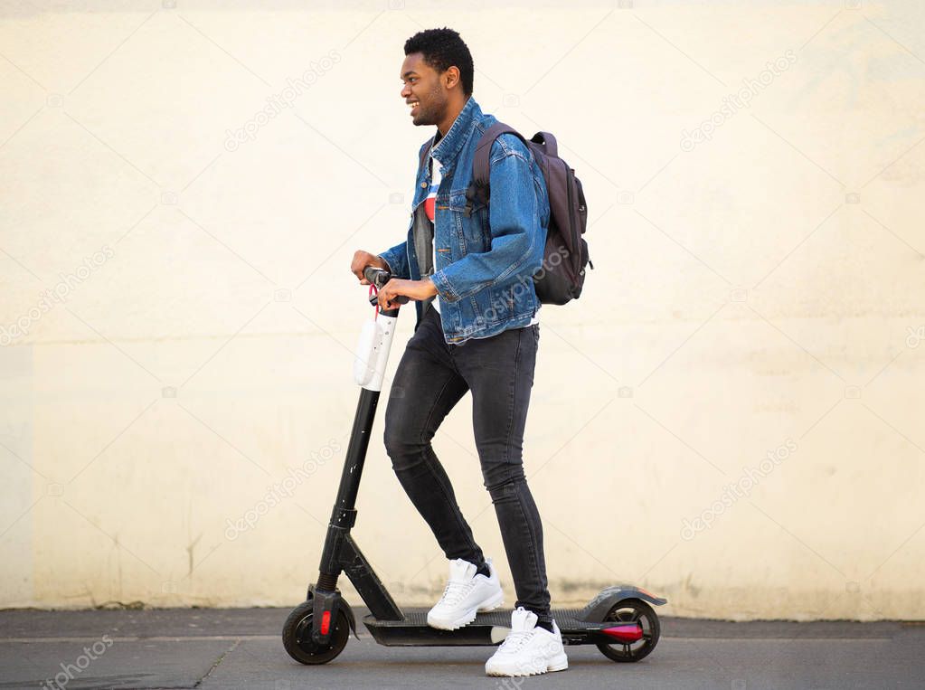 Full body side portrait happy african American guy on mobile scooter on street